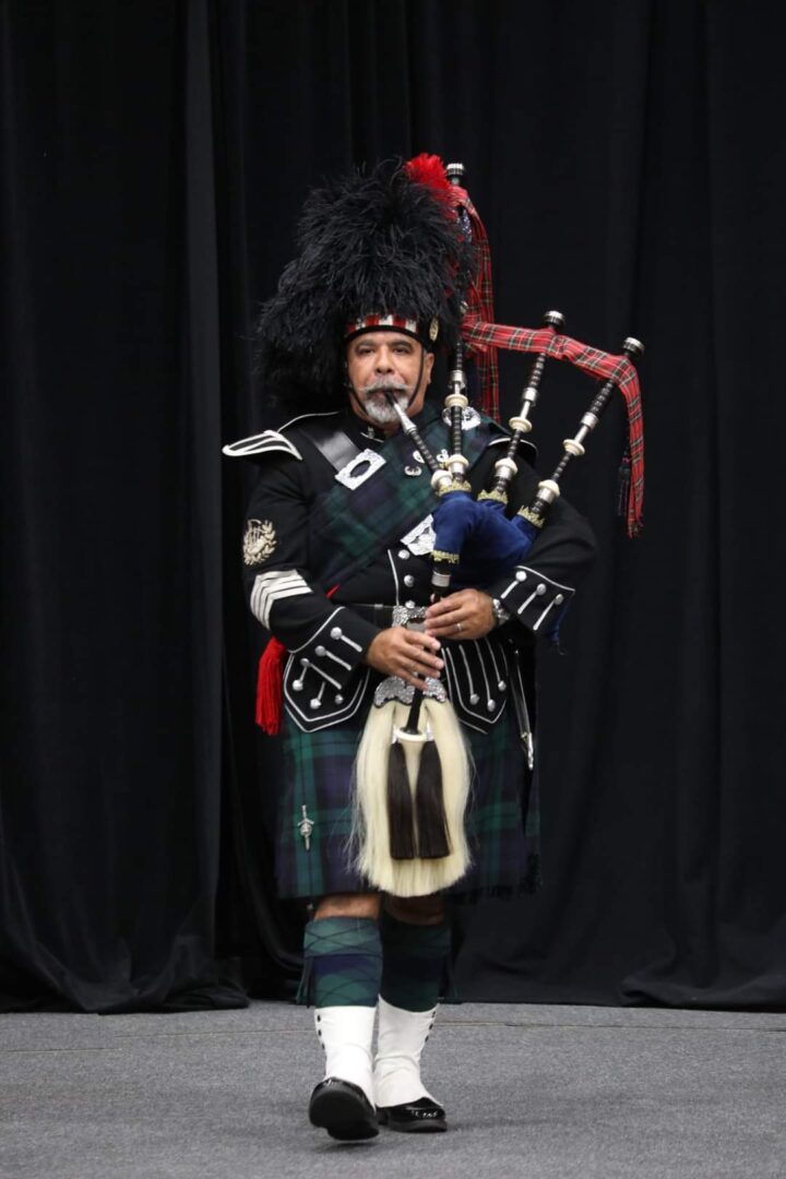 A man in a kilt and hat playing the bagpipes.