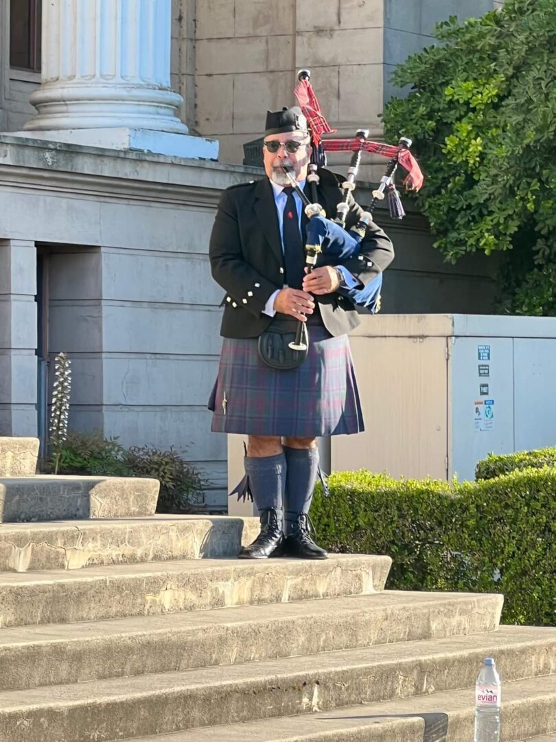 A man in a kilt and bagpipe stands on steps.