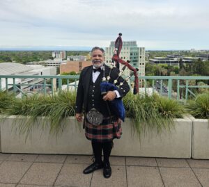 A man in a kilt and bagpipe stands on the roof of an apartment building.