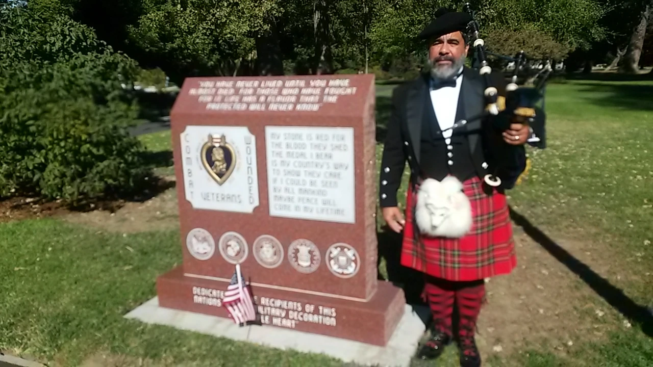 A man in a kilt and hat standing next to a memorial.